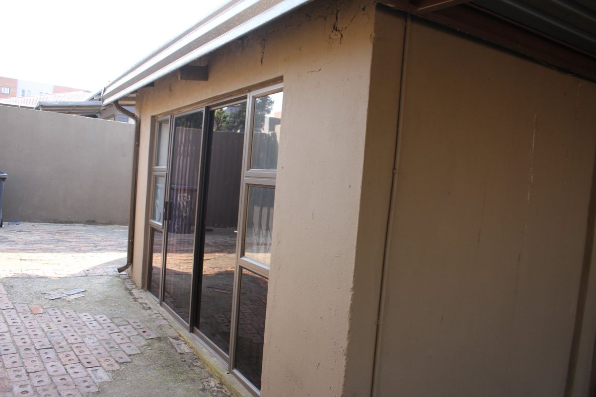 Rear exterior view of the property featuring sliding glass doors, metal guttering, and a paved courtyard area with boundary walls.