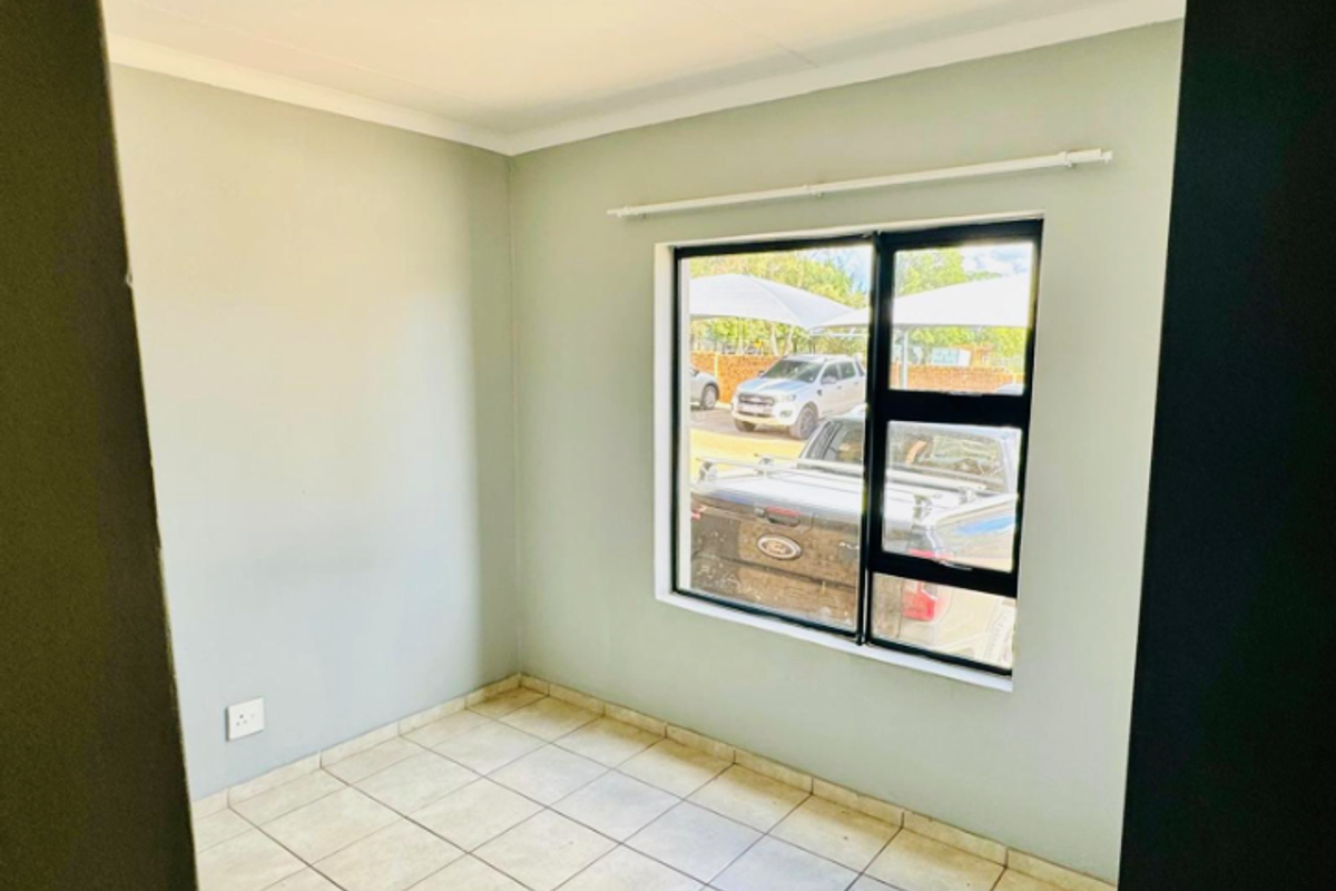 A clean, empty bedroom featuring neutral wall paint, tiled flooring, and an aluminium-framed window with a curtain rail.