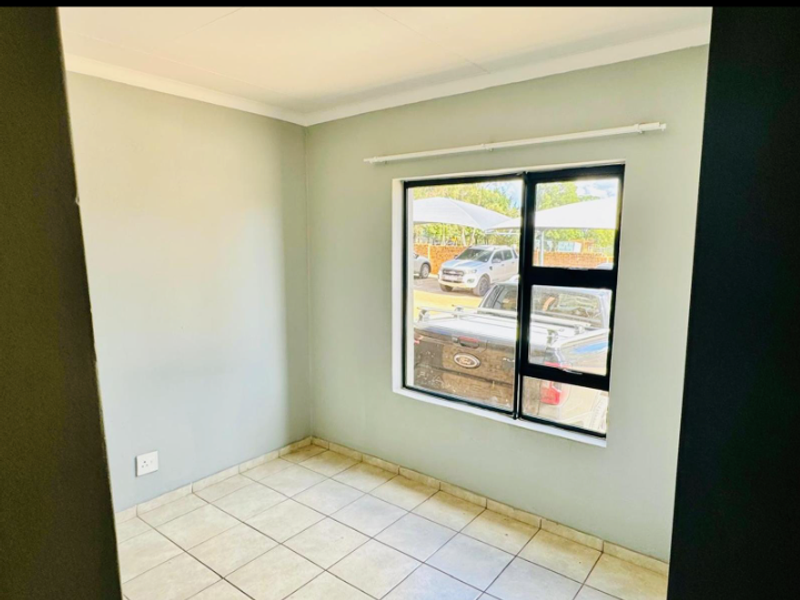 A clean, empty bedroom featuring neutral wall paint, tiled flooring, and an aluminium-framed window with a curtain rail.