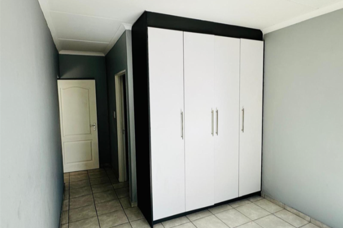 A clean, empty bedroom featuring neutral grey walls, tiled flooring, and a modern built-in wardrobe with white doors and black framing.