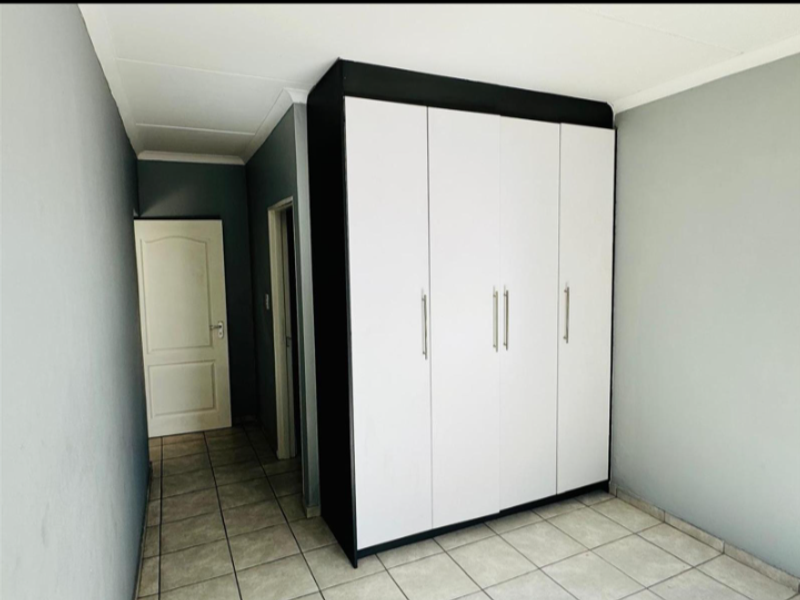A clean, empty bedroom featuring neutral grey walls, tiled flooring, and a modern built-in wardrobe with white doors and black framing.