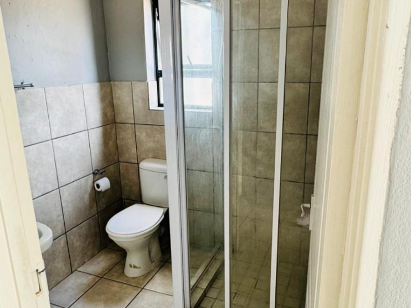 A functional bathroom featuring a shower enclosure and toilet, with tiled finishes. The ceiling shows signs of water damage requiring repair.