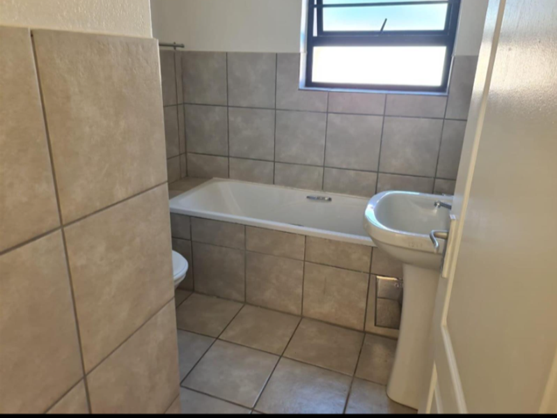 A functional bathroom featuring a bathtub, pedestal basin, toilet, and neutral floor-to-ceiling tiling with a top-hung window for natural light.