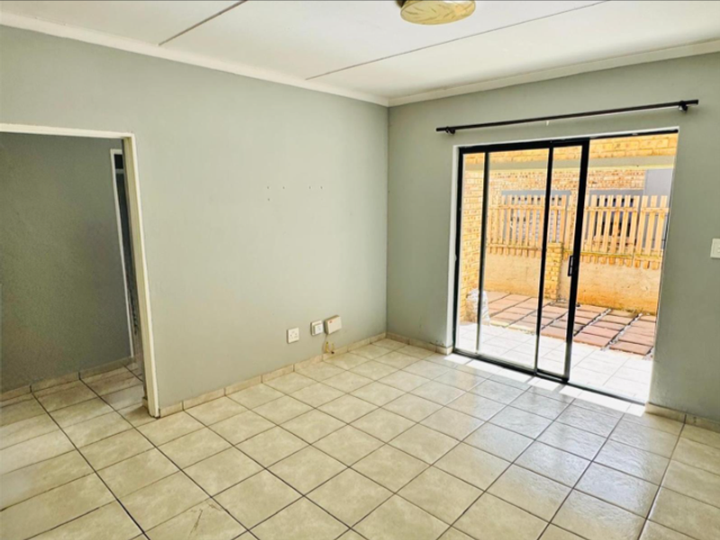 An empty living room featuring tiled flooring and a sliding glass door providing direct access to an outdoor patio area.