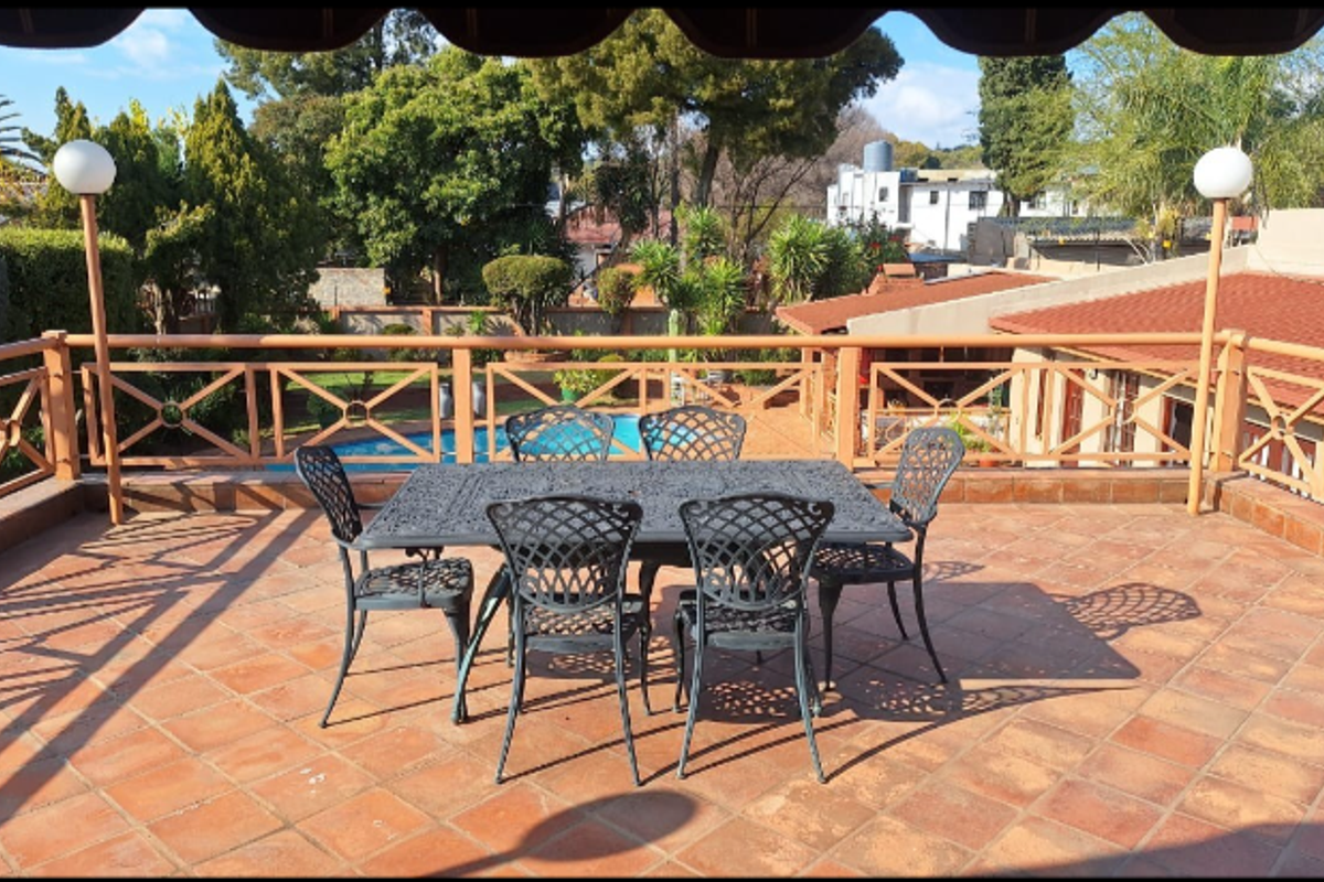 Spacious elevated balcony featuring terracotta tiling and a wooden balustrade, overlooking the garden and swimming pool area.