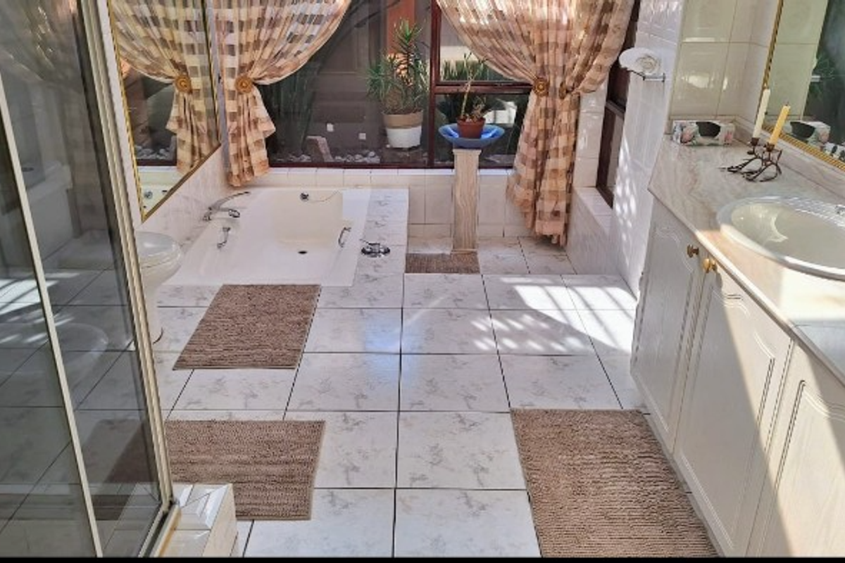 Spacious bathroom featuring a built-in bathtub, double vanity with marble-look countertop, glass shower enclosure, and large wall-to-wall mirrors.