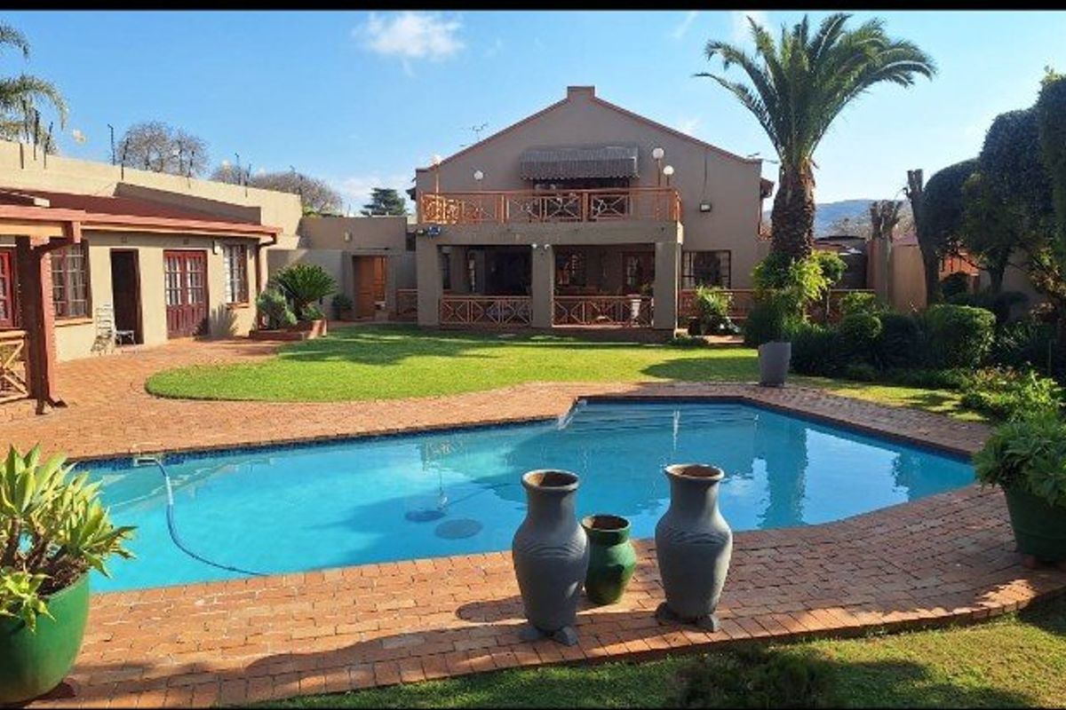 Spacious rear garden featuring a swimming pool, brick-paved patio area, and a two-story dwelling with a covered ground-floor patio and upper-level balcony.