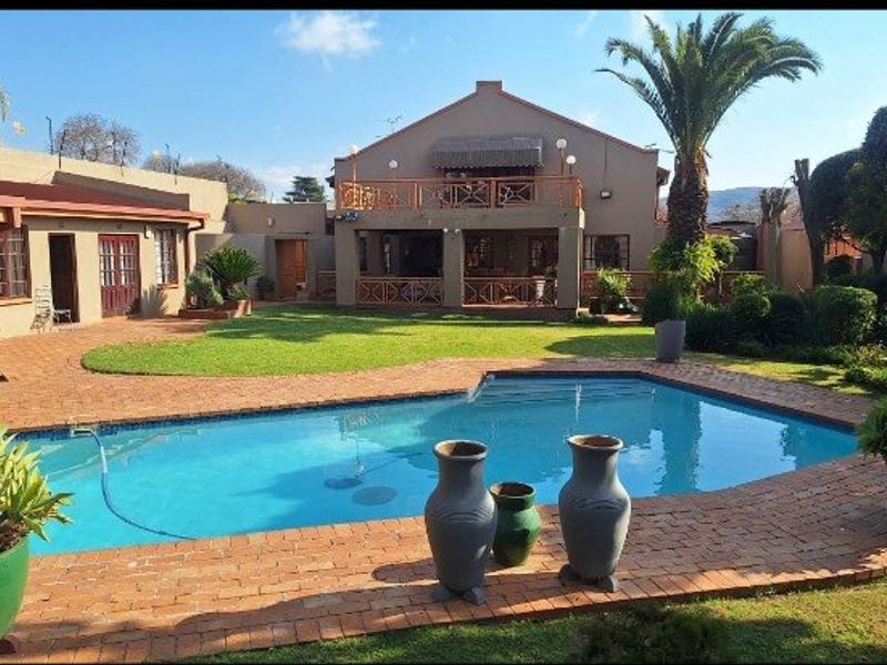 Spacious rear garden featuring a swimming pool, brick-paved patio area, and a two-story dwelling with a covered ground-floor patio and upper-level balcony.