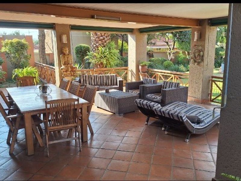 A spacious covered patio featuring tiled flooring and a wooden balustrade, overlooking a landscaped garden area.