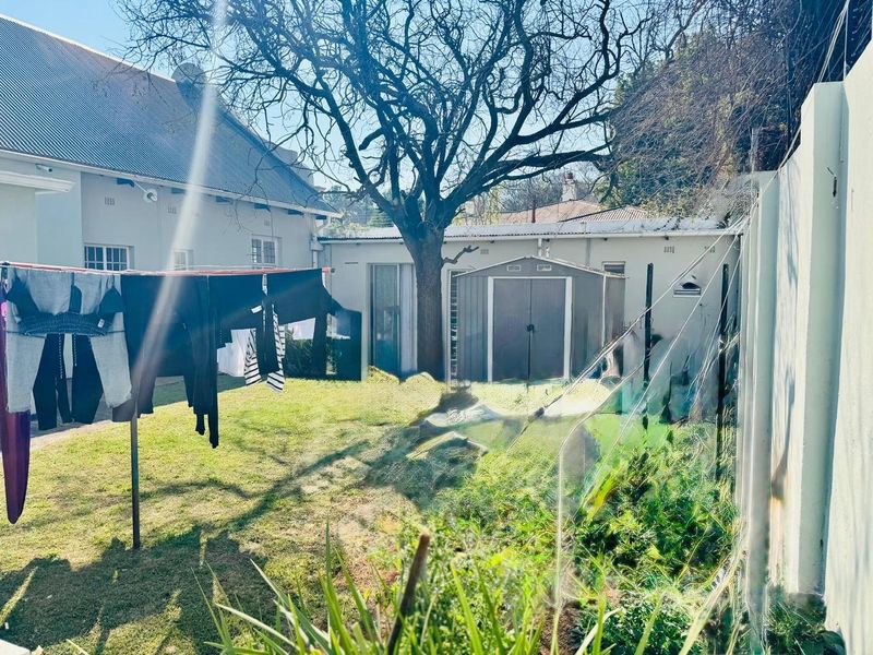 A rear garden area featuring a lawn, mature tree, and a storage shed, enclosed by a boundary wall.