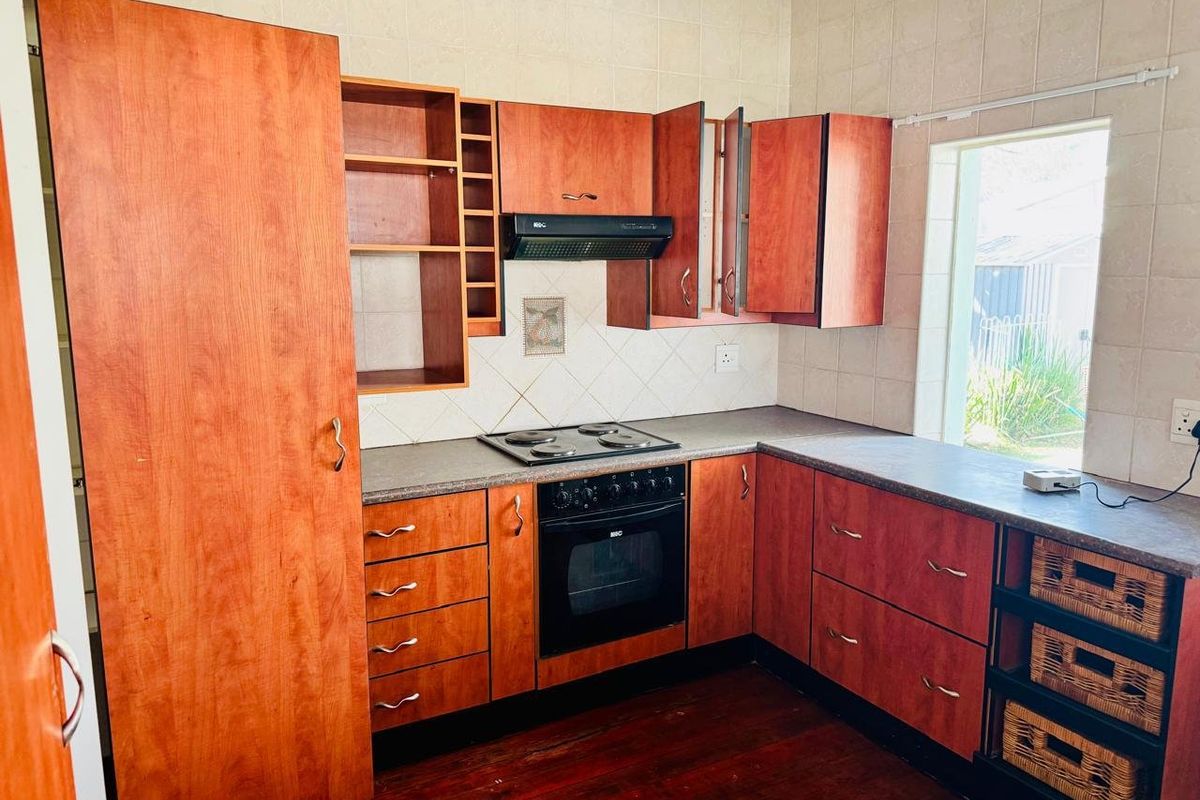 A functional kitchen featuring wood-tone cabinetry, laminate countertops, built-in oven, electric hob, and extractor fan, complemented by tiled backsplash and timber flooring.