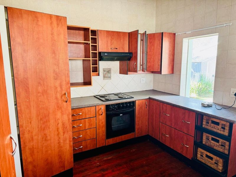 A functional kitchen featuring wood-tone cabinetry, laminate countertops, built-in oven, electric hob, and extractor fan, complemented by tiled backsplash and timber flooring.