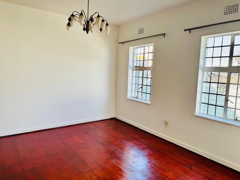 An empty living room featuring polished hardwood flooring, leaded glass windows, and a classic ceiling light fixture.
