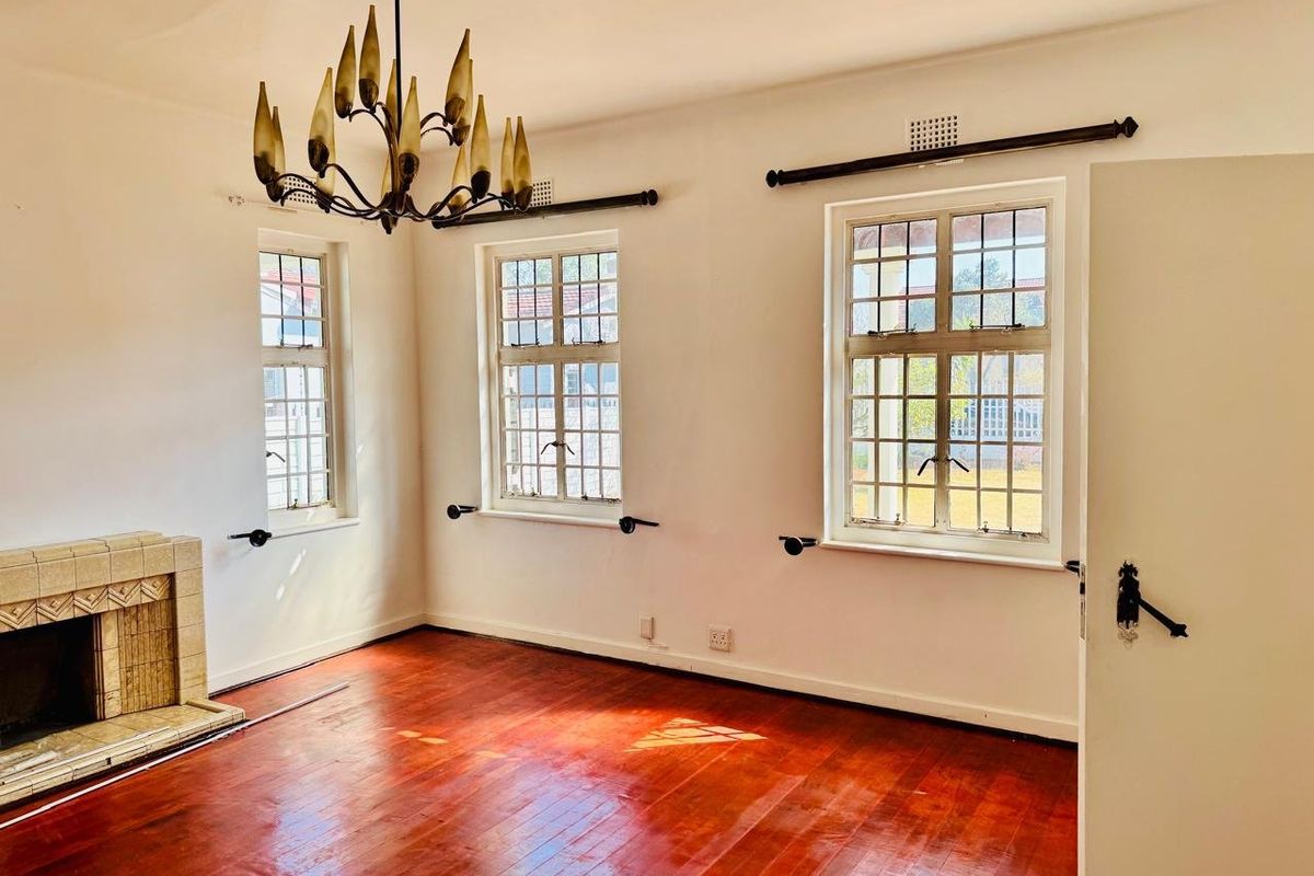 A bright, empty living room featuring original hardwood floors, a classic tiled fireplace, and charming leaded glass windows.