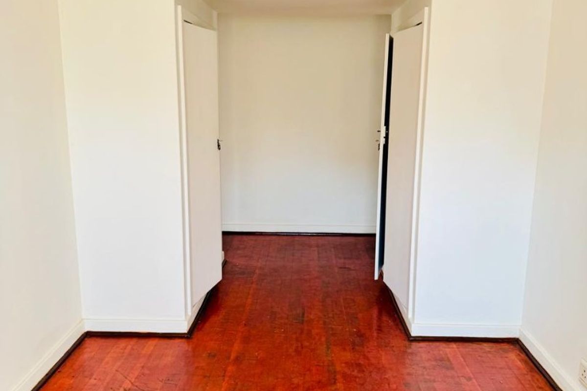 An empty bedroom featuring original hardwood flooring and a built-in cupboard, offering a blank canvas for renovation.