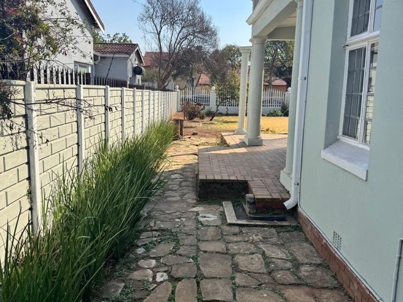 Rear exterior view featuring a stone paved pathway, brick patio with classical columns, and a precast concrete boundary wall.