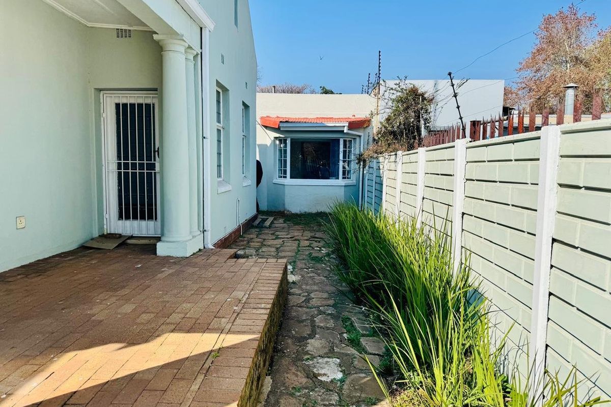 Rear exterior view featuring a brick paved patio, stone walkway, and a precast concrete boundary wall with established garden greenery.