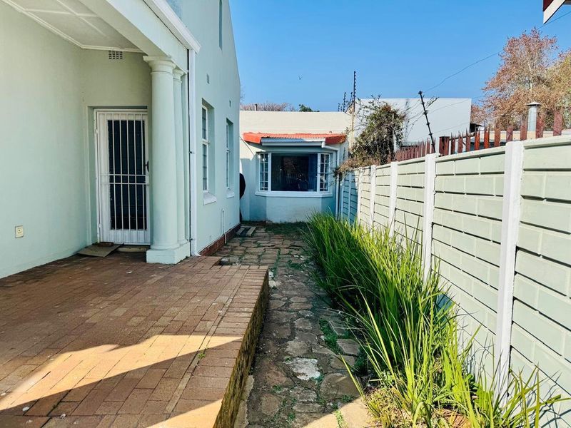 Rear exterior view featuring a brick paved patio, stone walkway, and a precast concrete boundary wall with established garden greenery.