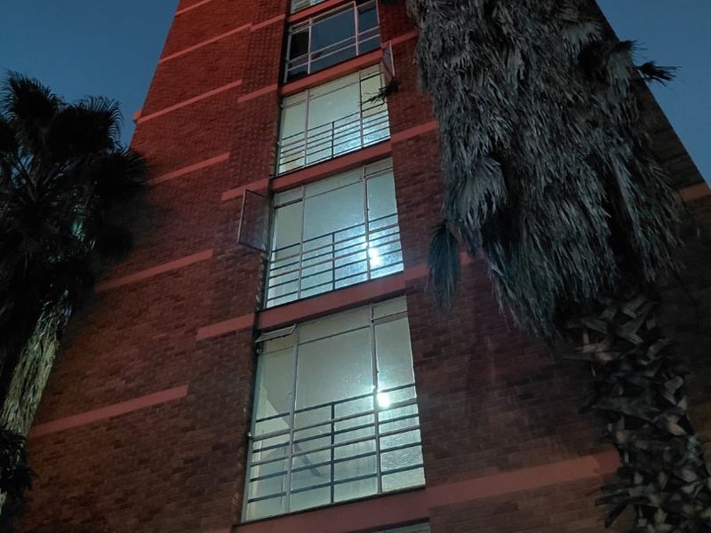 Low-angle night view of a multi-story brick apartment building featuring large windows with security railings and perimeter electric fencing.