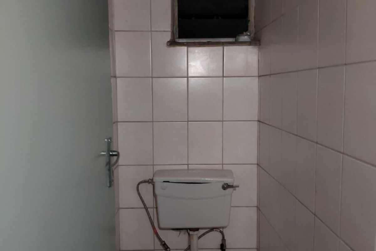 A small, dated bathroom featuring a standard toilet, full-height ceramic wall tiling, and a louvered window for ventilation.