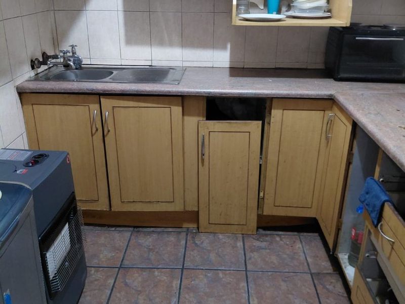 A dated kitchen featuring laminate cabinetry, tiled backsplash, and ceramic flooring, currently showing signs of wear and maintenance issues with the cabinetry.