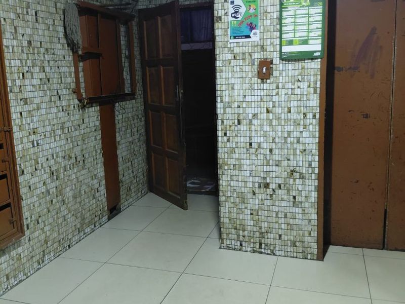 A communal apartment hallway featuring mosaic wall tiles, tiled flooring, and elevator access, showing signs of age and wear.