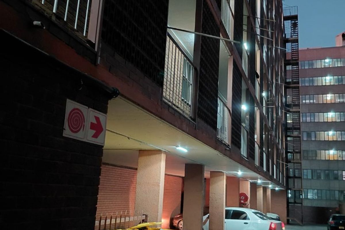 Exterior view of an apartment building featuring brick facade, concrete support pillars, and metal balcony railings at dusk.