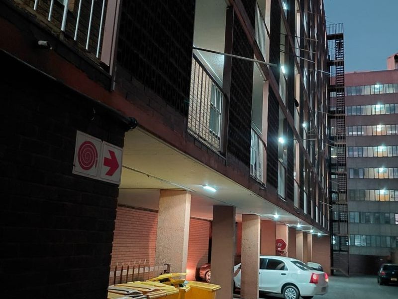 Exterior view of an apartment building featuring brick facade, concrete support pillars, and metal balcony railings at dusk.
