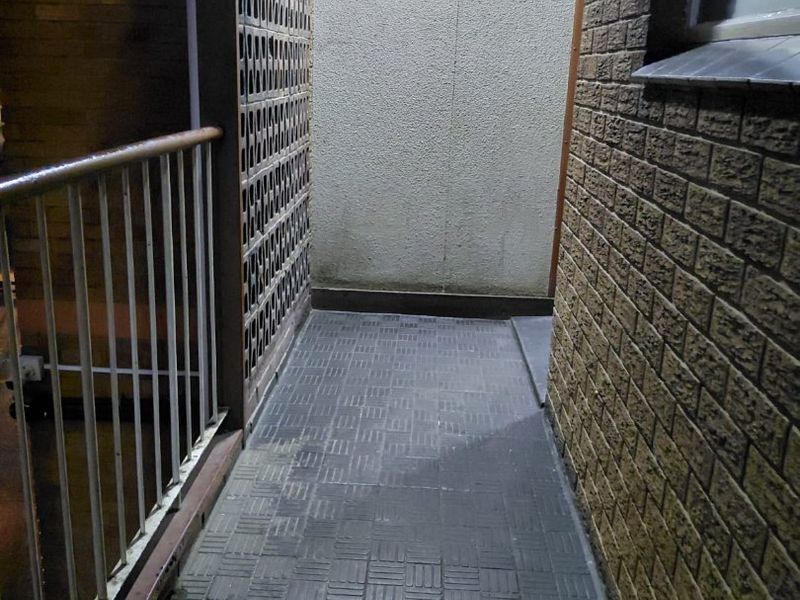 A narrow outdoor balcony area featuring a decorative breeze block screen, metal railing, and tiled flooring, providing a functional transition space.