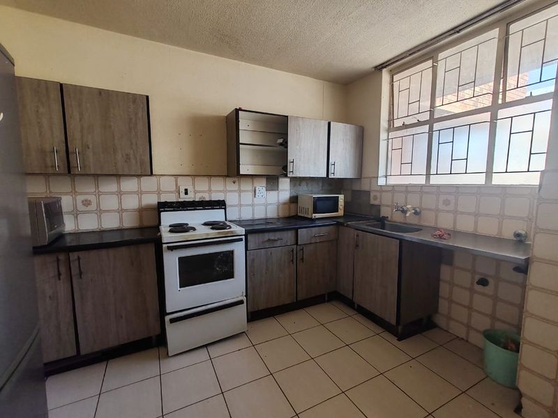 A functional kitchen featuring laminate cabinetry, tiled backsplash, and tiled flooring, requiring cosmetic updates to improve its overall condition and aesthetic appeal.