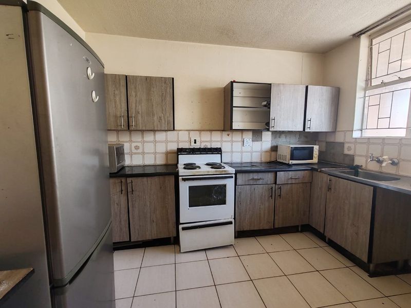 A functional kitchen featuring laminate cabinetry, tiled backsplash, ceramic flooring, and a freestanding stove, requiring cosmetic updates to improve its overall condition.