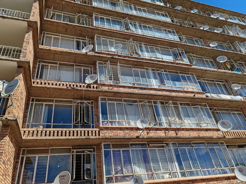 Exterior view of a multi-story apartment building facade featuring brick construction, metal-framed windows, and multiple satellite dishes installed on the exterior.