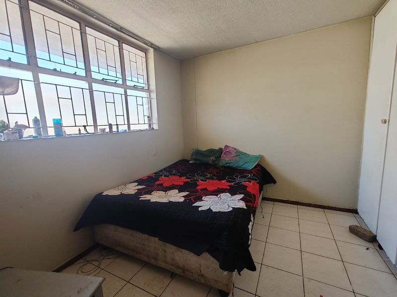 A bedroom featuring tiled flooring, a built-in wardrobe, and large windows with security bars, offering a functional space in need of cosmetic updates.