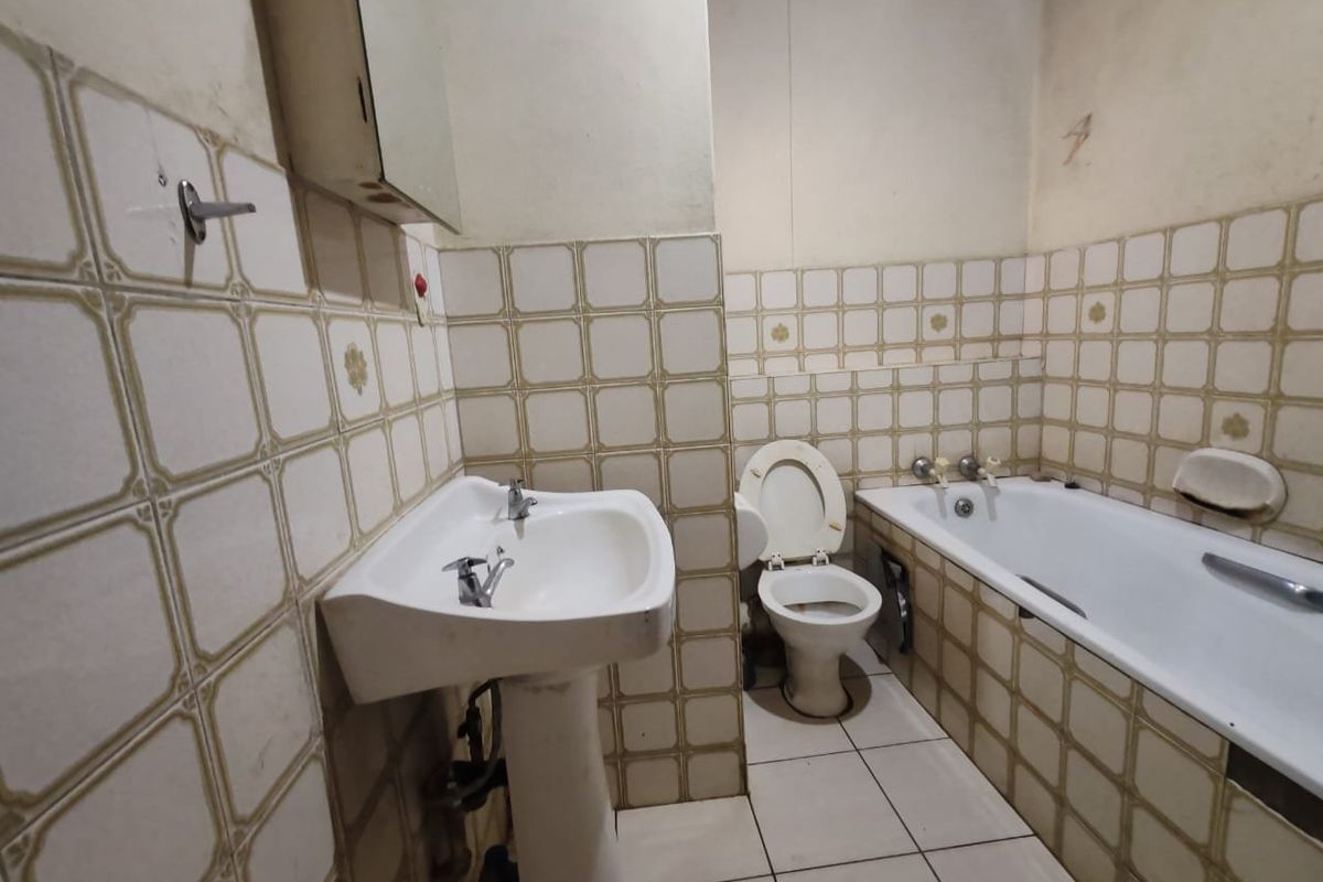 A dated bathroom featuring a pedestal basin, bathtub, and toilet with original ceramic tiling throughout, requiring modernization and cosmetic updates.