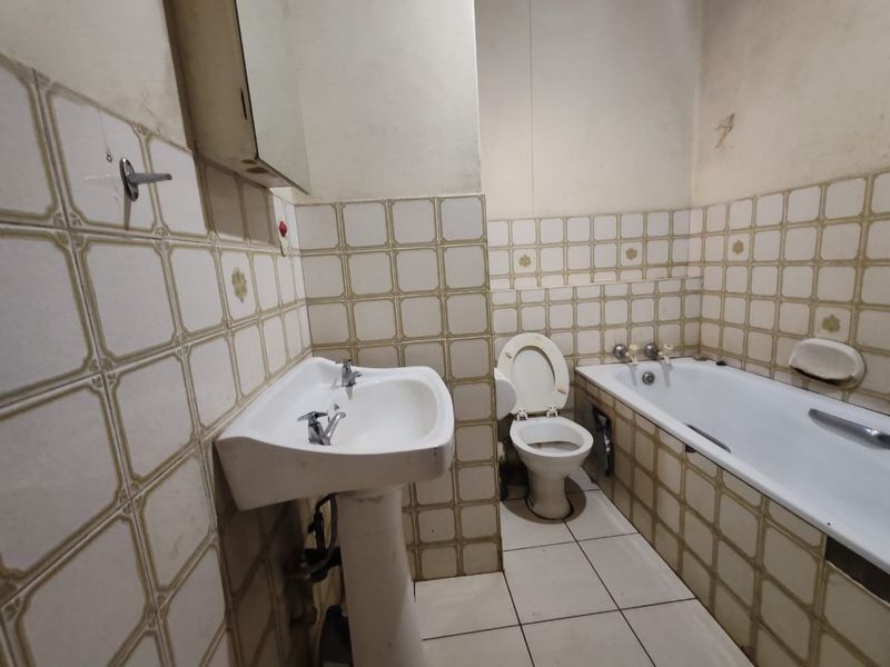 A dated bathroom featuring a pedestal basin, bathtub, and toilet with original ceramic tiling throughout, requiring modernization and cosmetic updates.