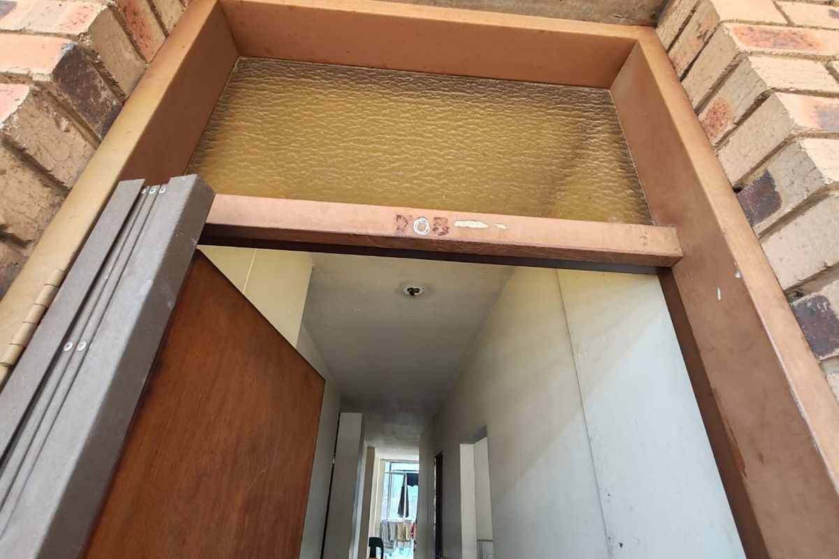 View of the apartment entrance featuring a brick facade and a timber door frame with a transom window above the doorway.