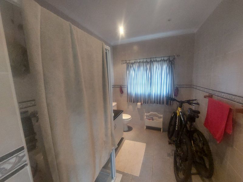 A functional bathroom featuring tiled walls and flooring, a shower enclosure, and a vanity cabinet, providing a practical layout for daily use.