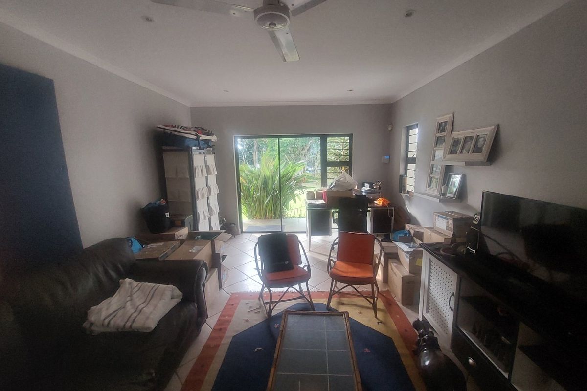 A living room featuring tiled flooring, a ceiling fan, and a sliding glass door providing access to the outdoor area.