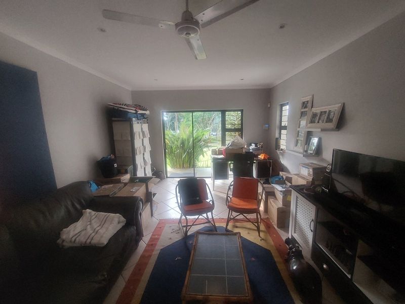 A living room featuring tiled flooring, a ceiling fan, and a sliding glass door providing access to the outdoor area.