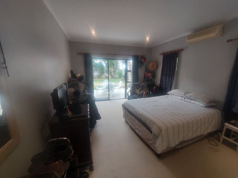 Spacious bedroom featuring neutral carpeting, recessed lighting, a wall-mounted air conditioner, and sliding glass doors providing direct access to the outdoor patio area.
