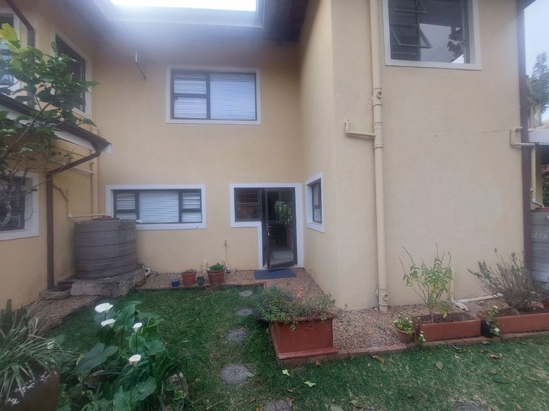 Rear exterior view of the apartment featuring a small garden area, gravel landscaping, and external water storage tank.