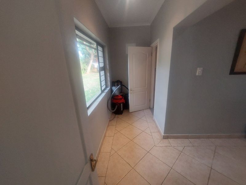 A functional hallway featuring tiled flooring, a window with security bars, and access to an internal door.