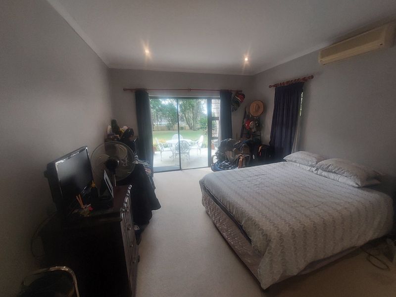 Spacious bedroom featuring neutral walls, carpeted flooring, a wall-mounted air conditioning unit, and sliding glass doors providing direct access to the outdoor patio area.