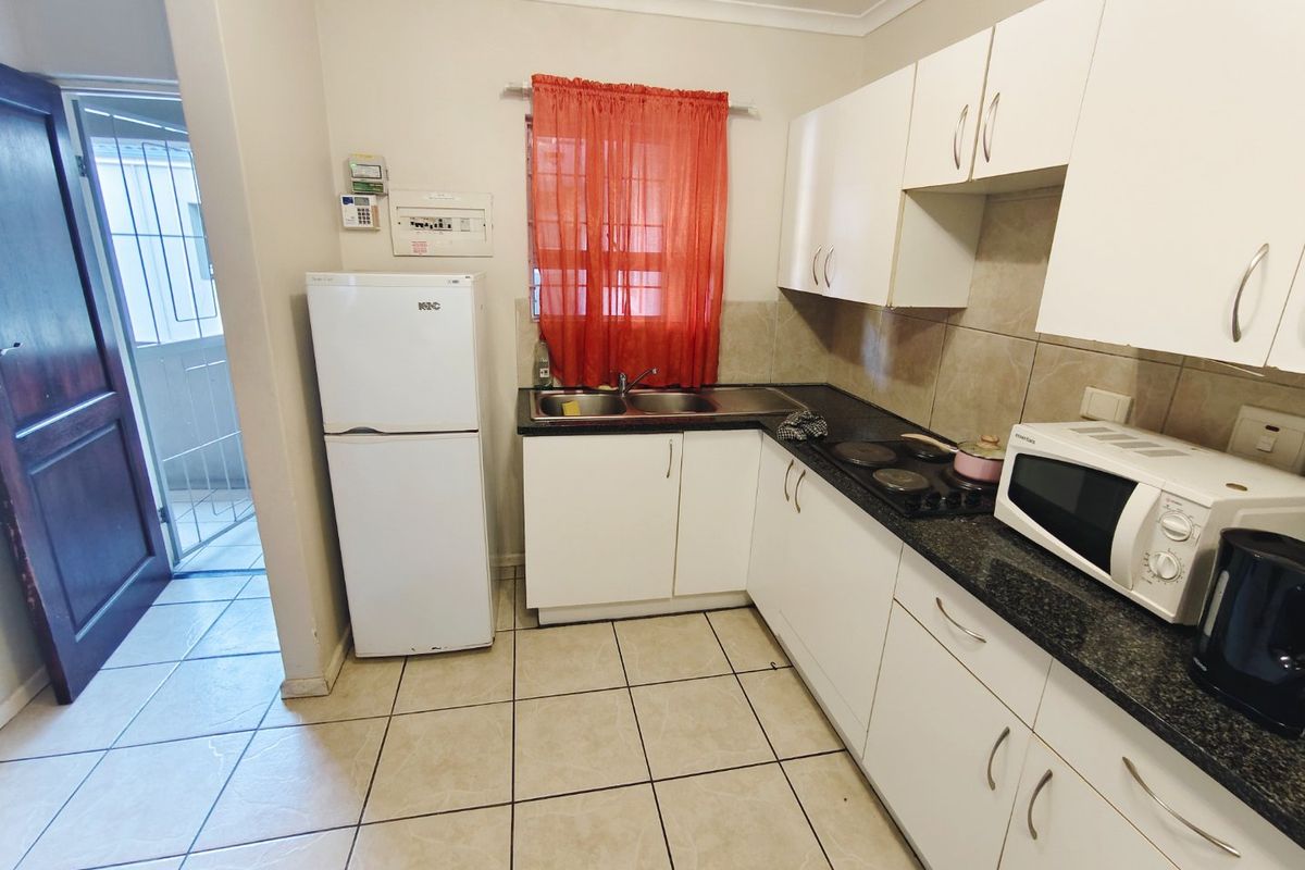 Compact kitchen featuring white built-in cabinetry, dark granite countertops, a double basin sink, electric hob, and tiled flooring with direct access to an exterior area.