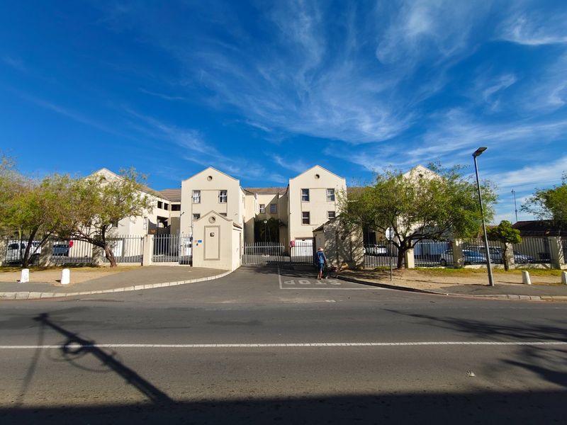 Front elevation of an apartment complex featuring a gated entrance, security fencing, and paved driveway access from the street.