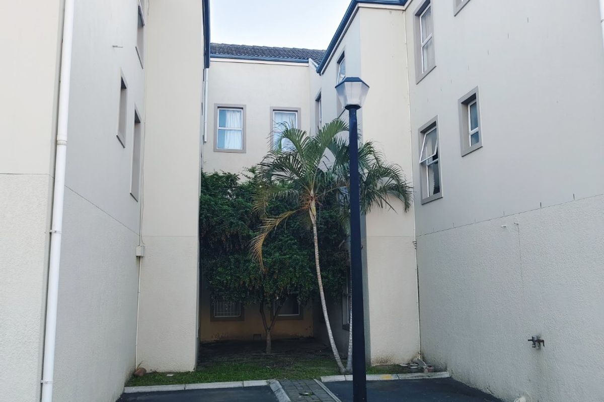 A view of the rear exterior area of the apartment complex, featuring an asphalt driveway, paved median, and established landscaping.