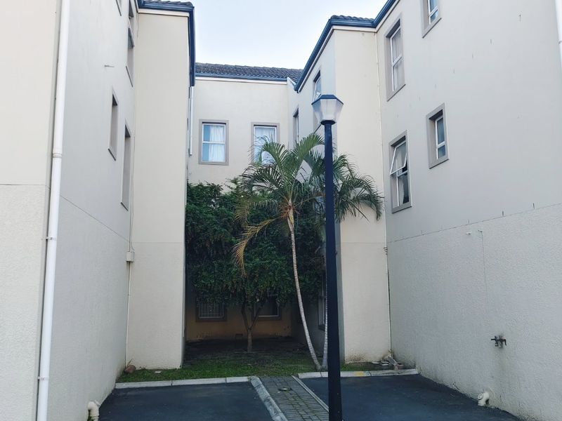 A view of the rear exterior area of the apartment complex, featuring an asphalt driveway, paved median, and established landscaping.