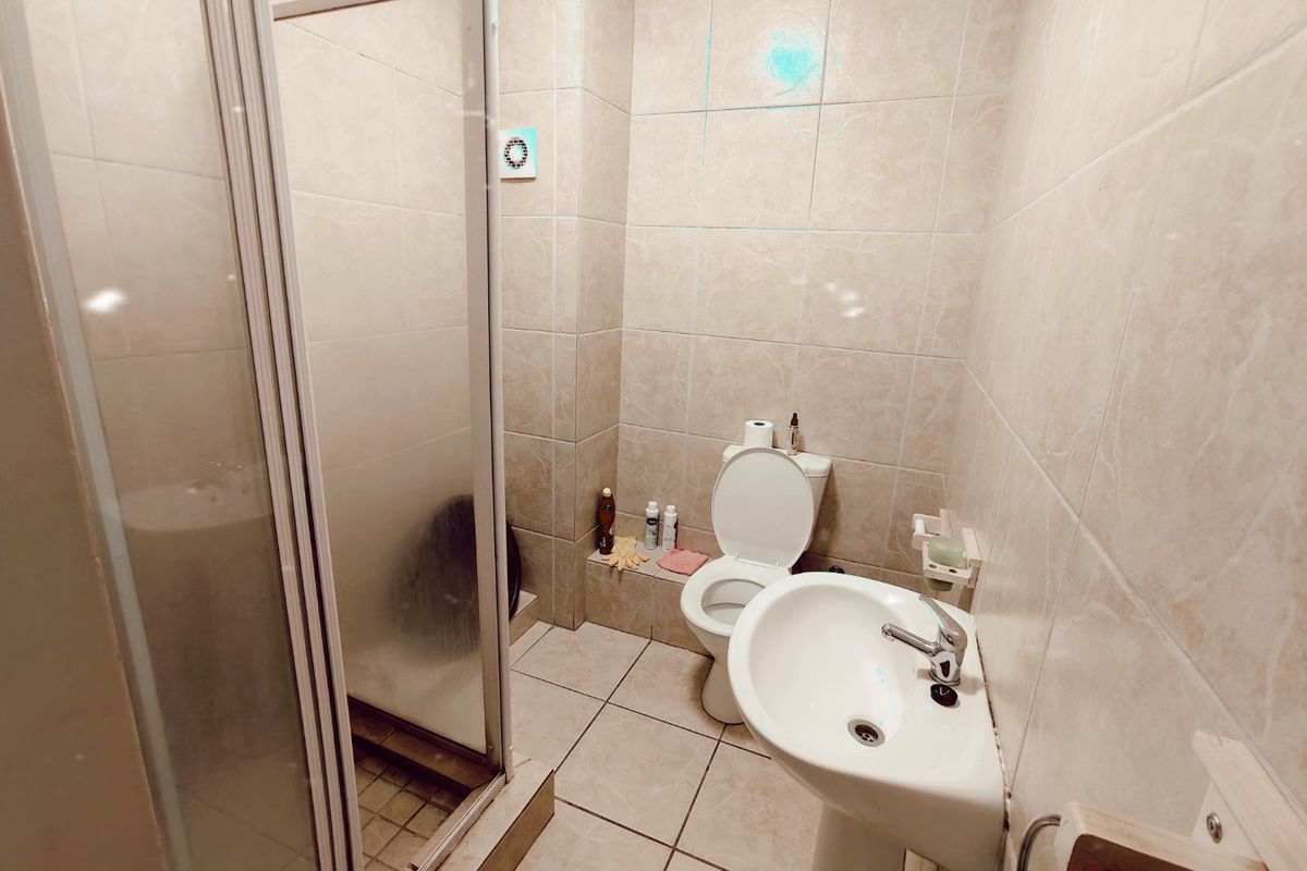 A functional bathroom featuring a shower enclosure, pedestal basin, and toilet, finished with neutral wall and floor tiling.