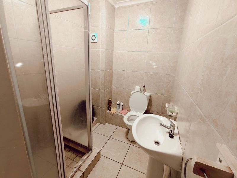 A functional bathroom featuring a shower enclosure, pedestal basin, and toilet, finished with neutral wall and floor tiling.