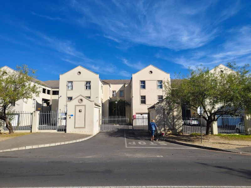 Front elevation of a multi-story apartment complex featuring secure gated access, paved driveway, and well-maintained exterior facade.